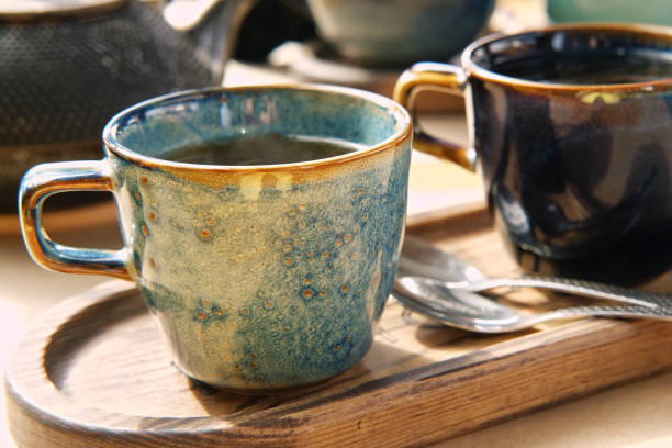 istock Brewing and Serving Tea. Teapot Pouring Green Tea in Blue Ceramic Cup on Wooden Cafe Table. Two Pottery Handmade Mugs Early in the Morning. Trendy Authentic Porcelain Set. Breakfast Concept. Tea Time. 1498371349