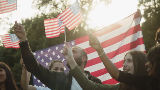 A group of people is waving small American flags at sunset