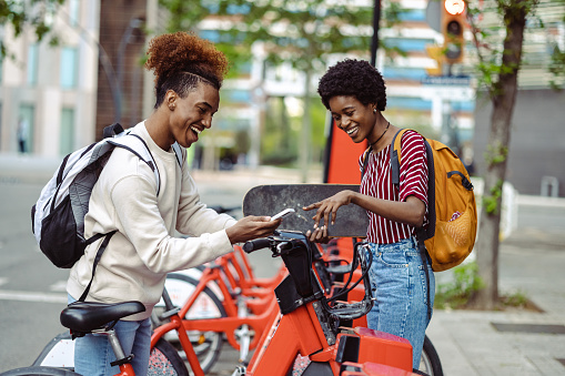 Cheerful African American young people in an urban part of the city. They are using public bicycles in the city