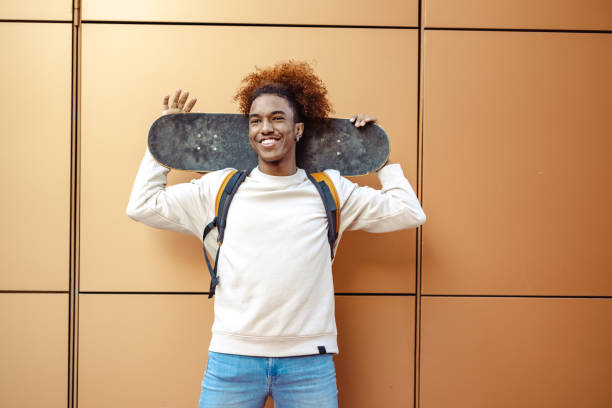 istock Young urban man with a skateboard against an orange wall 1498390271