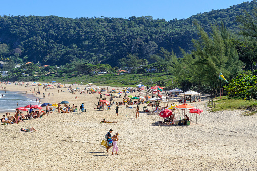 Itaipu, Rio de Janeiro, Brazil - June 9, 2023: Itacoatiara Beach. Group of people outdoors enjoying the sand and water in the local landmark.