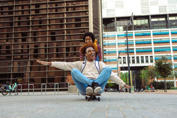 Cheerful African American young people in urban part of the city. They are using skateboard and having fun
