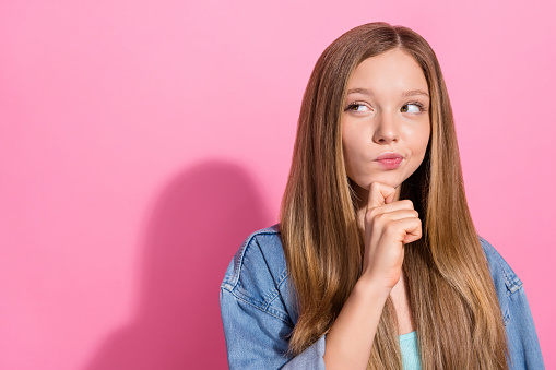Photo portrait of pretty young teen girl touch chin look cunning empty space dressed stylish denim outfit isolated on pink color background.