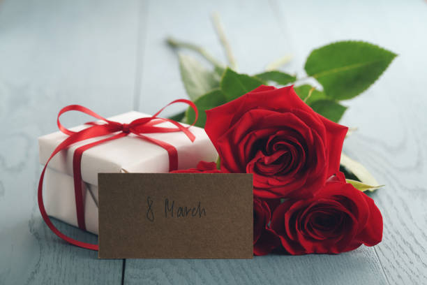 istock three red roses on blue wood table with gift and 8 march paper card 1498393916