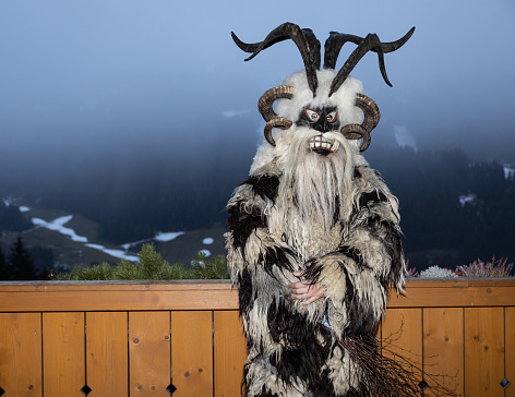 Krampus, the hero of Christmas legends, in a skin and a horned mask stands at a wooden fence against a background of fog, Austria, Gastein. High quality photo