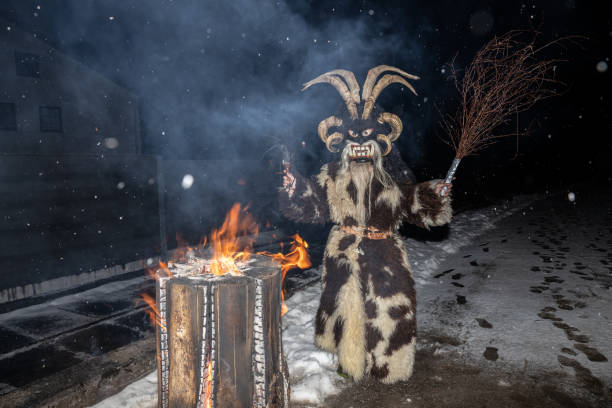 le diable de noël krampus avec des tiges à la main se tient à une souche brûlante par une nuit enneigée, autriche, gastein - mythology snow winter austria photos et images de collection