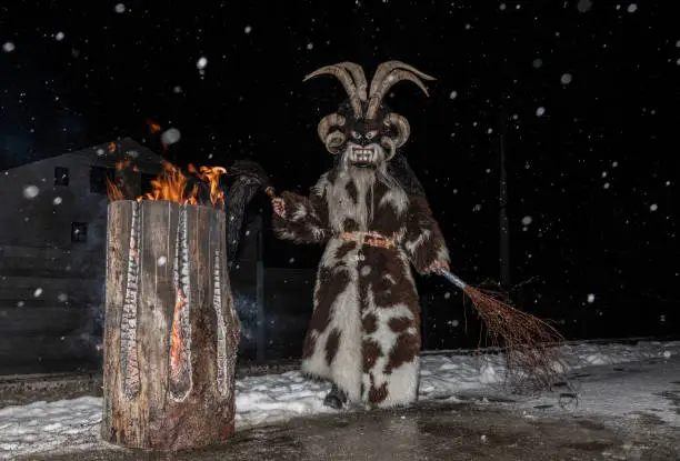 The legendary Christmas krampus stands by a living fire on a snowy night, Austria, Gastein. High quality photo