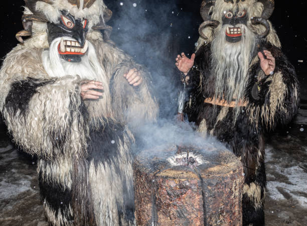 deux krampus de noël se réchauffant les mains par une nuit enneigée près d’un arbre fumant, autriche, gastein - mythology snow winter austria photos et images de collection