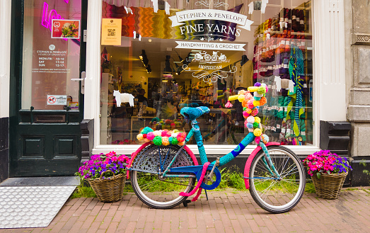 Amsterdam, Netherlands-June 2, 2023-A bicycle, parked outside a yarn shop in Amsterdam, is almost completely covered with crochet and handknit yarn including its chain lock and saddle.