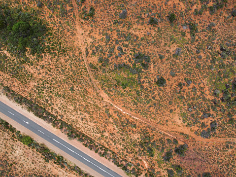 Aerial shot of a road in a dry, desert landscape with the colour being predominantly orange with a few green shrubs also a view of a small dirt road for walking., Klein Karoo.
