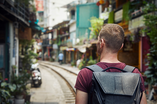 Man with a backpack walking through narrow Train Street. Railroad track between residential buildings in Hanoi Vietnam.