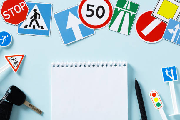 Driving school exam concept. Blank paper notebook, pen, road signs and traffic symbols on color background. stock photo