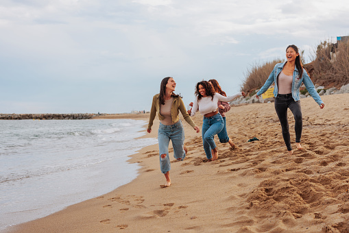 Four diverse happy young girls running joyfully on the beach shore.