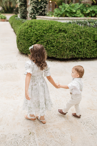 istock Lifestyle Candid Moment of a Brother & Sister Walking Together Holding Hands Wearing Sage Green & White Spring Wear in Palm Beach, Florida in May of 2023, Cuban-American 4-Year-Old Toddler Girl & 1-Year-Old Baby Boy Both with Light Brown Hair 1498410092