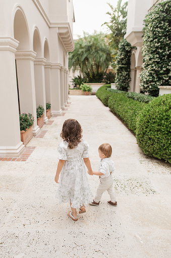 istock Lifestyle Candid Moment of a Brother & Sister Walking Together Holding Hands Wearing Sage Green & White Spring Wear in Palm Beach, Florida in May of 2023, Cuban-American 4-Year-Old Toddler Girl & 1-Year-Old Baby Boy Both with Light Brown Hair 1498410094