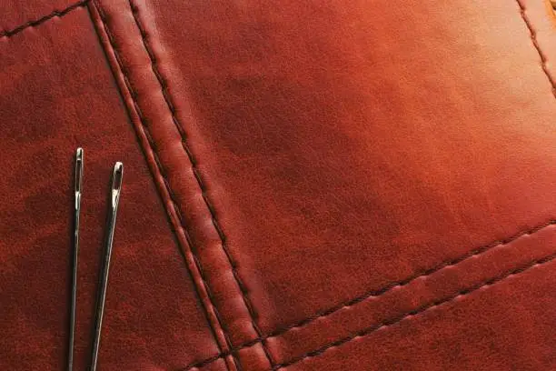 Close-up of a brown leather surface with a variety of sewing tools neatly laid out on top, including a measuring tape, scissors, and thimble