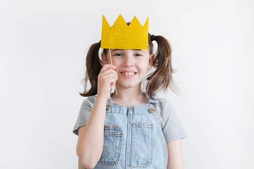 Beautiful little girl with paper crown posing on white background