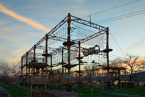 Wide-angle landscape view of Rope adventure attraction in the park near Dnipro River in Kyiv, Ukraine. Designed for beginners among the children. Sunset sky in the background.