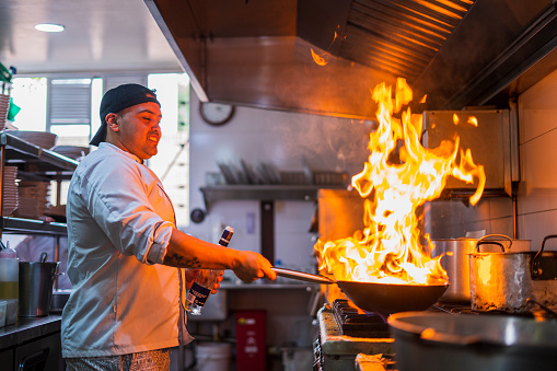 Chef of Latin ethnicity between the ages of 30-40 is preparing a frying pan in a kitchen