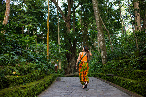 Rear view of a young woman walking along the footpath in Bali, Ubud, Indonesia. The footpath is treelined and shes the only person in the image.