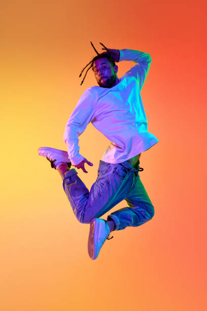 istock Young bearded man with dreads in casual clothes dancing breakdance against gradient orange yellow studio background in neon light 1498420771