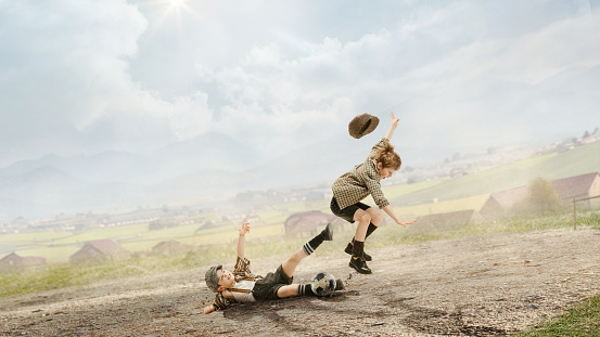 Happy, playful, little boys, children in retro style clothes playing football outdoors on a daytime. Countryside view. Concept of sport, childhood, retro style, active lifestyle, summer vacation