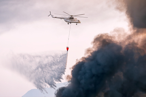 Firefighting aircraft extinguishing forest fire in hilly landscape with dropping water in inaccessible area