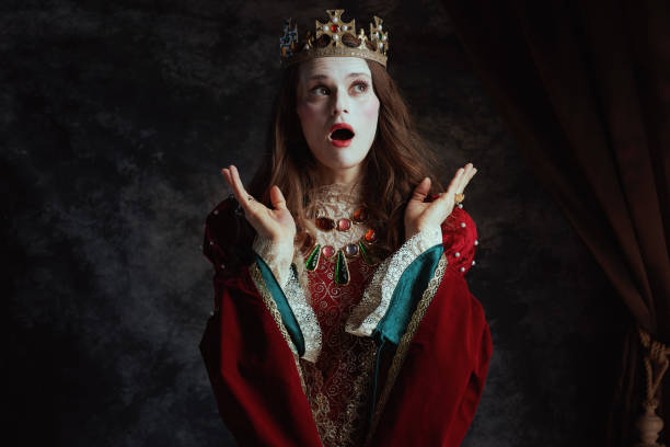 shocked medieval queen in red dress with white makeup shocked medieval queen in red dress with white makeup and crown on dark gray background. stage actress stock pictures, royalty-free photos & images