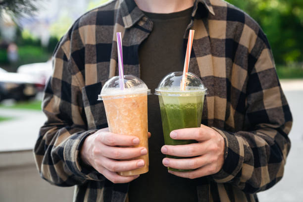 istock Man outdoors holding plastic cups with green and orange smoothies, close up. 1498424136