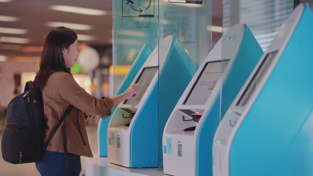 Asian woman passenger traveler using Scanning Boarding Passes Machine with passport and touching screen monitor digital display at the airport gates