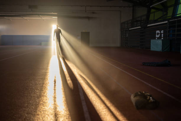 日光と暗い屋内スタジアムを歩くスポーツマン - sports track track and field stadium sport night ストックフォトと画像