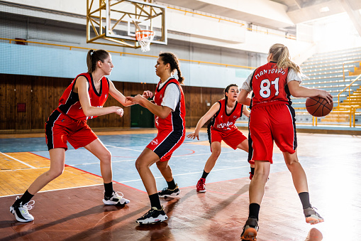 Basketball female team dribbling ball while training at indoors sports court wide shot