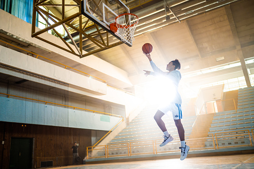 Male african american basketball player throwing ball in hoop while training at indoor sports court