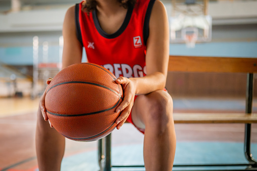 Female basketball player holding ball and sitting on bench at indoors court