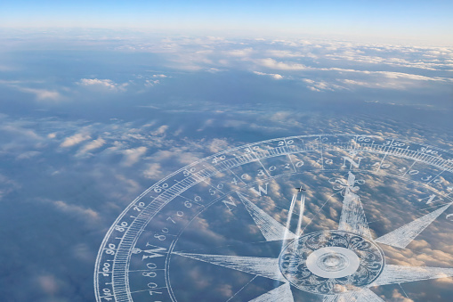 A compass points the way as contrails follow a jet airplane as it streaks above the clouds on the way to its destination.