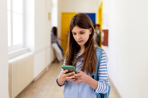 Serious Elementary School Female Using Smartphone in the Middle of the Corridor
