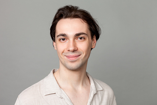 Studio portrait of a young white men in a beige shirt against a gray background