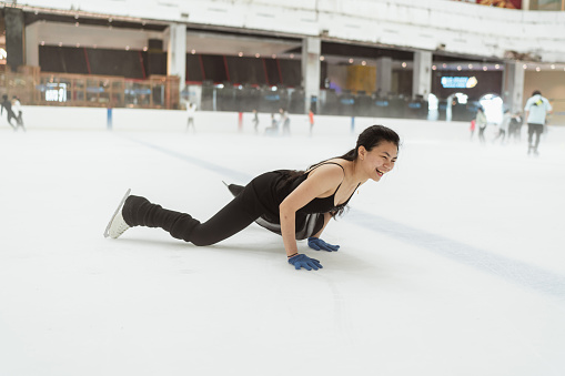 Asian female figure skater in black leotard takes a fall happily during practice