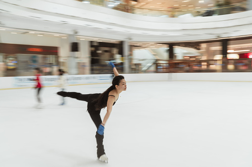 Asian female figure skater in black leotard practicing her skate routines