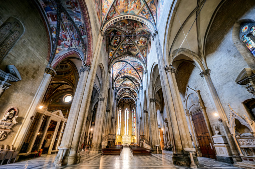 An imposing view of the splendid central nave and vaults of the Duomo in the medieval heart of Arezzo in Tuscany. Officially named as the Cattedrale dei Santi Pietro e Donato (Cathedral of Saints Peter and Donato), the Duomo of Arezzo was built starting from 1278 in the Italian Gothic style. The interior has three naves covered with cross vaults and divided by round Gothic arches. Inside are kept masterpieces by Donatello, Piero della Francesca and Guillaume de Marcillat, the latter author of numerous stained glass windows and rose windows and the frescoes on the vaults. Arezzo, founded in Etruscan times and later becoming an important center of Ancient Rome, is famous for the innumerable artistic and architectural treasures of its medieval and Renaissance heart. Super wide angle image in high definition quality.