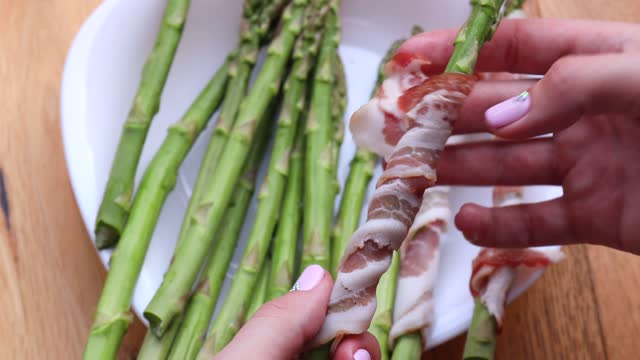 girl cook wraps asparagus in bacon. Cooking asparagus wrapped with bacon