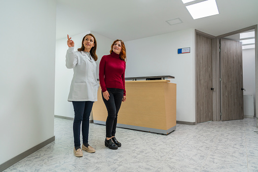 Latin woman doctor by profession dressed in her white coat in her medical office attends to a female patient who comes to her for medical treatment