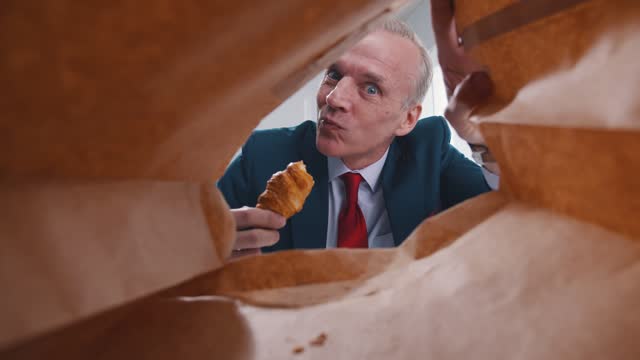 View from inside paper bag of mature businessman taking croissant for lunch a workplace