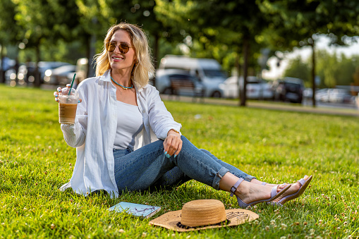 Woman relaxing in nature with an iced coffee and a book on a sunny summer day
