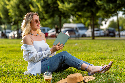 Woman relaxing in nature with an iced coffee and a book on a sunny summer day