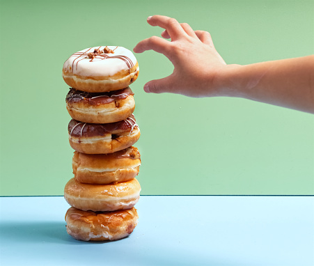 A child's hand is reaching for a stack of variety delicious donuts