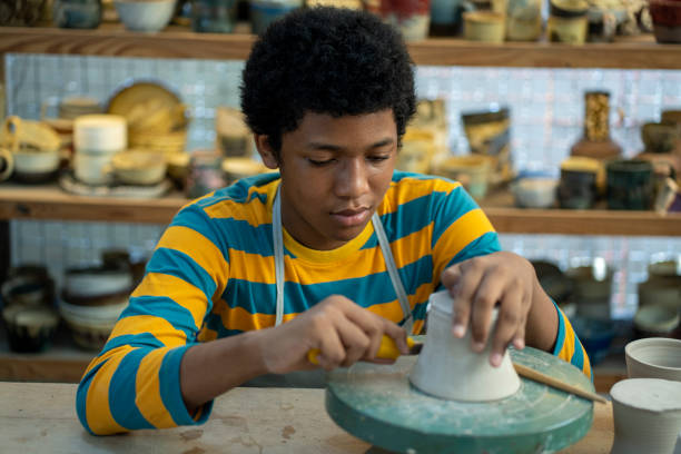 istock A talented young African American boy dons an apron in the workshop studio, his hands skillfully shaping pots and sculptures from mud and clay, bringing his artistic vision to life. 1498450478