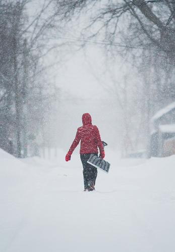 Woman in red jacket carries her shovel through a snowstorm
