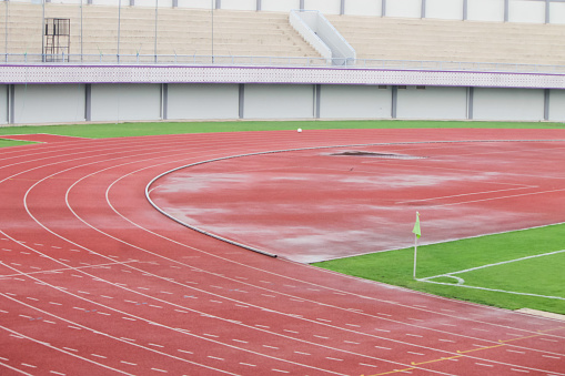 On the foreground you can see professional running tracks of a sport championship stadium. A long-range shot of a stadium field, floodlights and seating.  In the background are diffuse out-of-focus stadium seats with full bleachers. The whole image is made in 3D.
