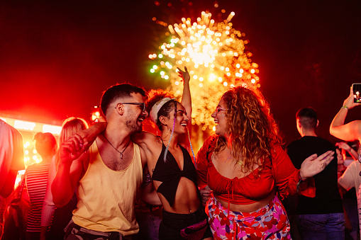 Three young happy friends are smiling, singing and dancing at a summer festival.